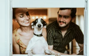 A black and white Italian Greyhound while standing between a woman and man.
